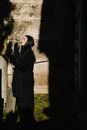 Side view of female in mourning black clothes and headscarf praying with closed eyes in cemetery