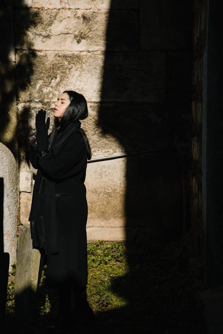 Woman Standing Near Gravestone And Praying