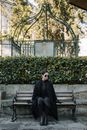 Full body of melancholic female in black mourning clothes and sunglasses sitting on bench