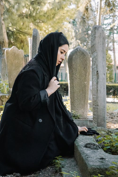 Woman in black headscarf sitting on grave