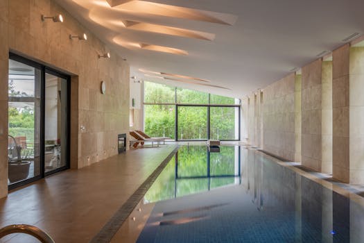 Deep swimming pool illuminated with lights in modern apartment with large windows in daytime