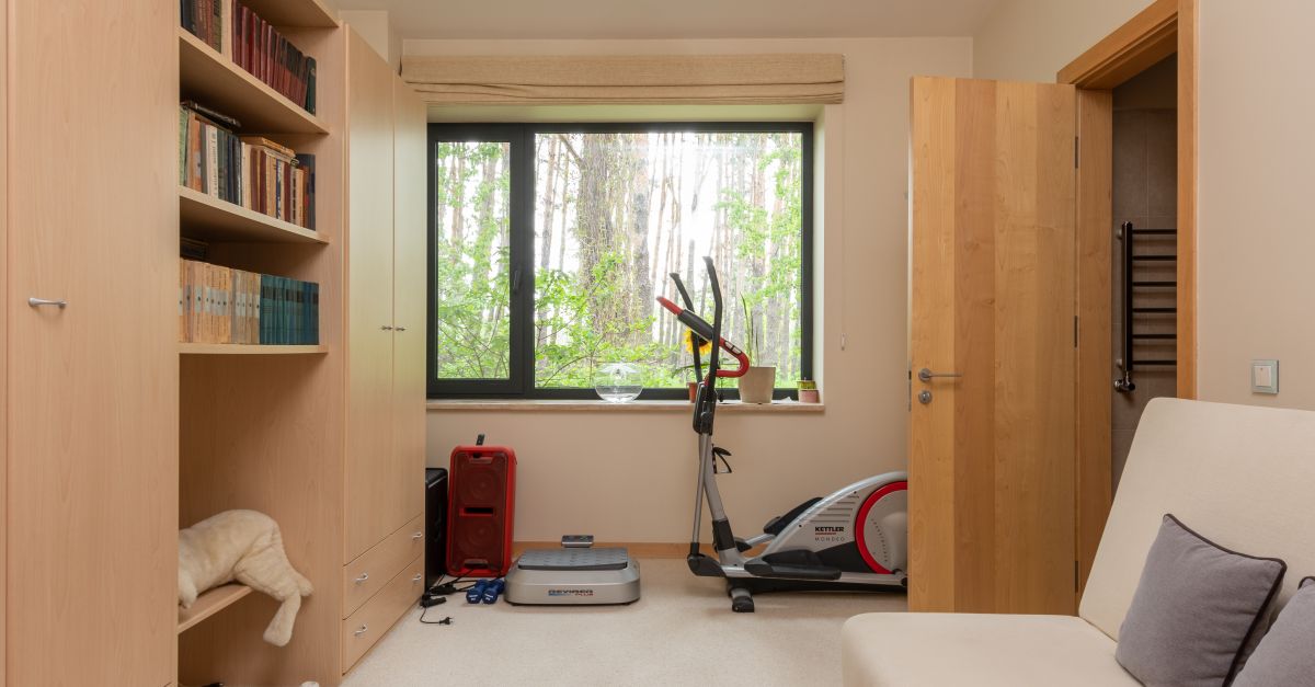 Contemporary apartment with many books and exercycle near wooden door and window in daytime