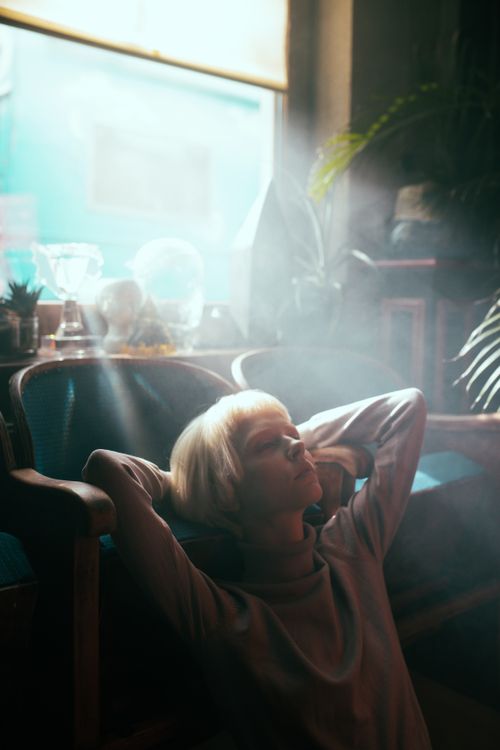 Free A serene moment of a woman lounging in an armchair, bathed in sunlight indoors. Stock Photo