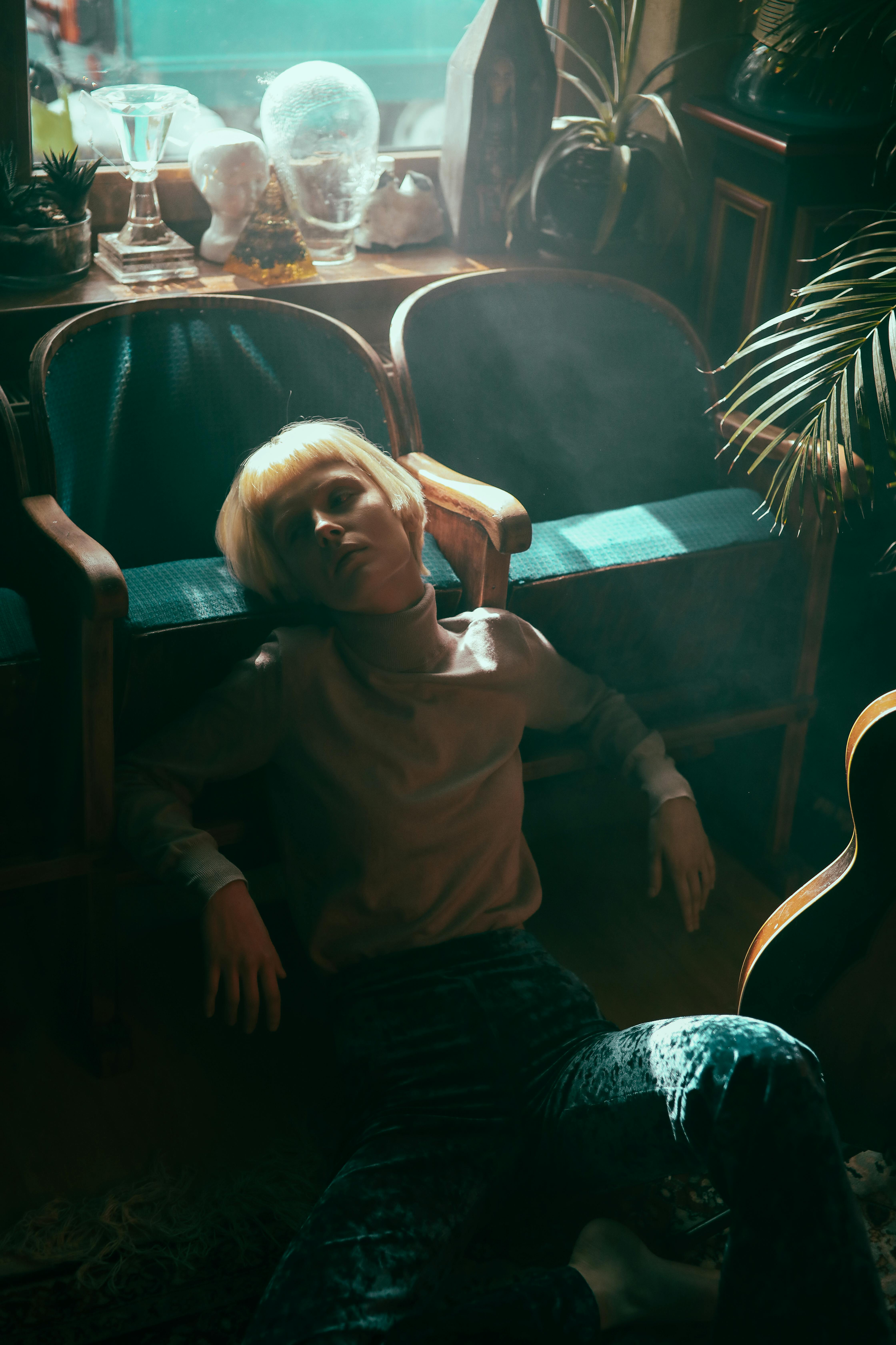 Moody portrait of a woman with blonde hair sitting indoors wearing a turtleneck sweater.