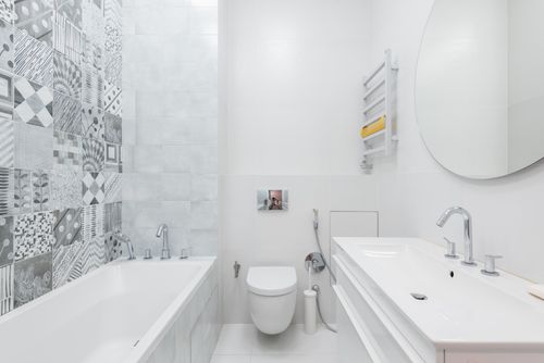 Free Contemporary bathroom featuring white sanitaryware, a round mirror, and patterned wall tiles for a sleek design. Stock Photo