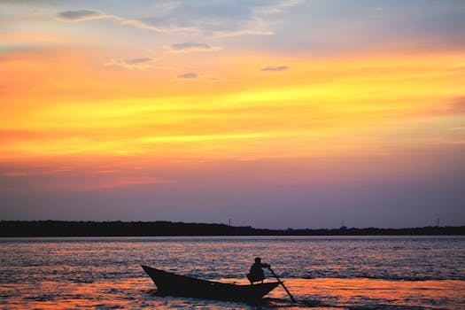 日落时分，渔民划船的剪影映衬在充满活力的天空和平静的水面上，构成一幅宁静的场景