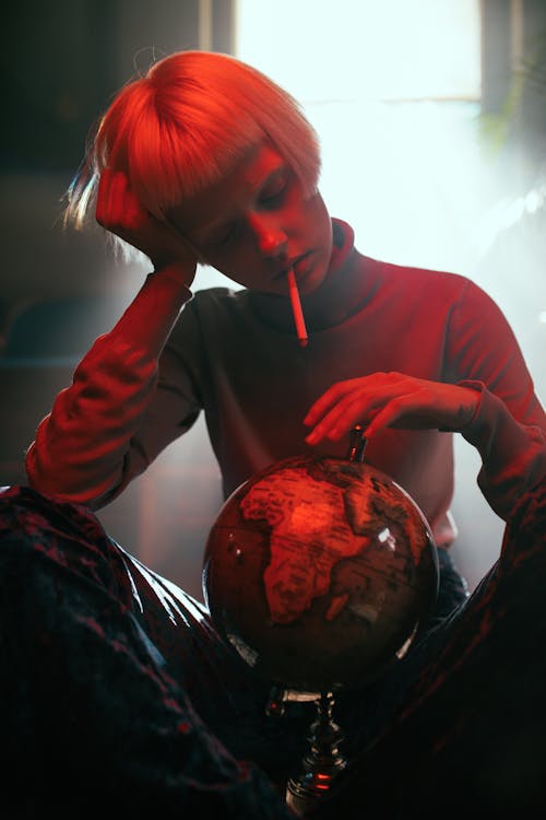 
A Woman in a Turtleneck Sweater Looking at a Globe while Smoking a Cigarette