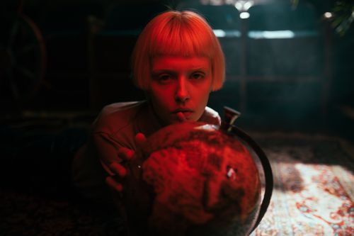 Free Artistic portrait of a woman with short blonde hair holding a globe under red lighting. Stock Photo