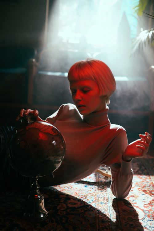 Free A woman with short blonde hair holds a globe, illuminated by moody light. Stock Photo