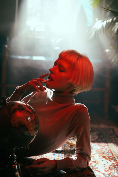 Free Stylish woman in turtleneck smoking beside globe in moody lighting. Stock Photo