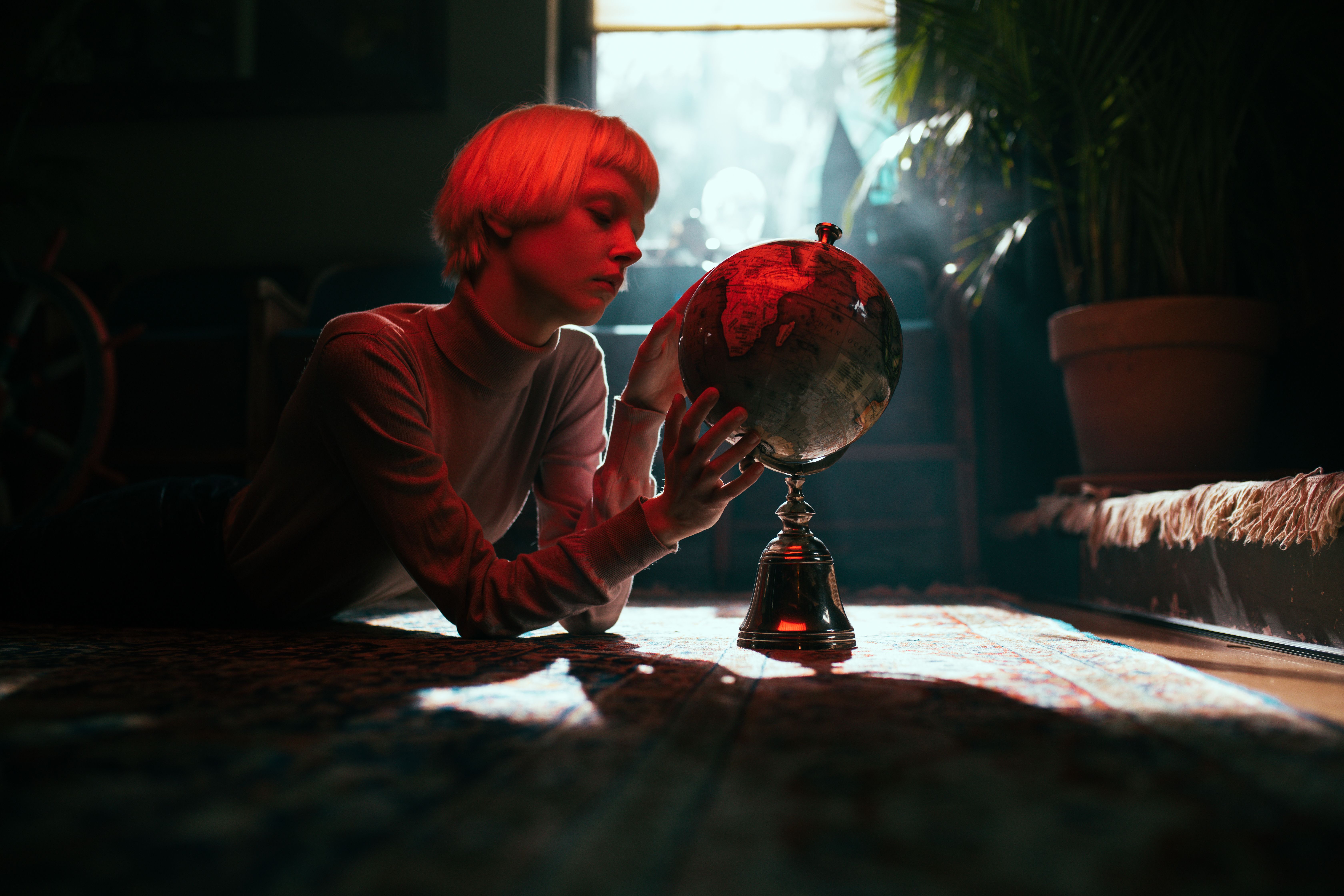 A young woman studies a globe in a warmly lit interior, creating an intriguing and thoughtful ambiance.