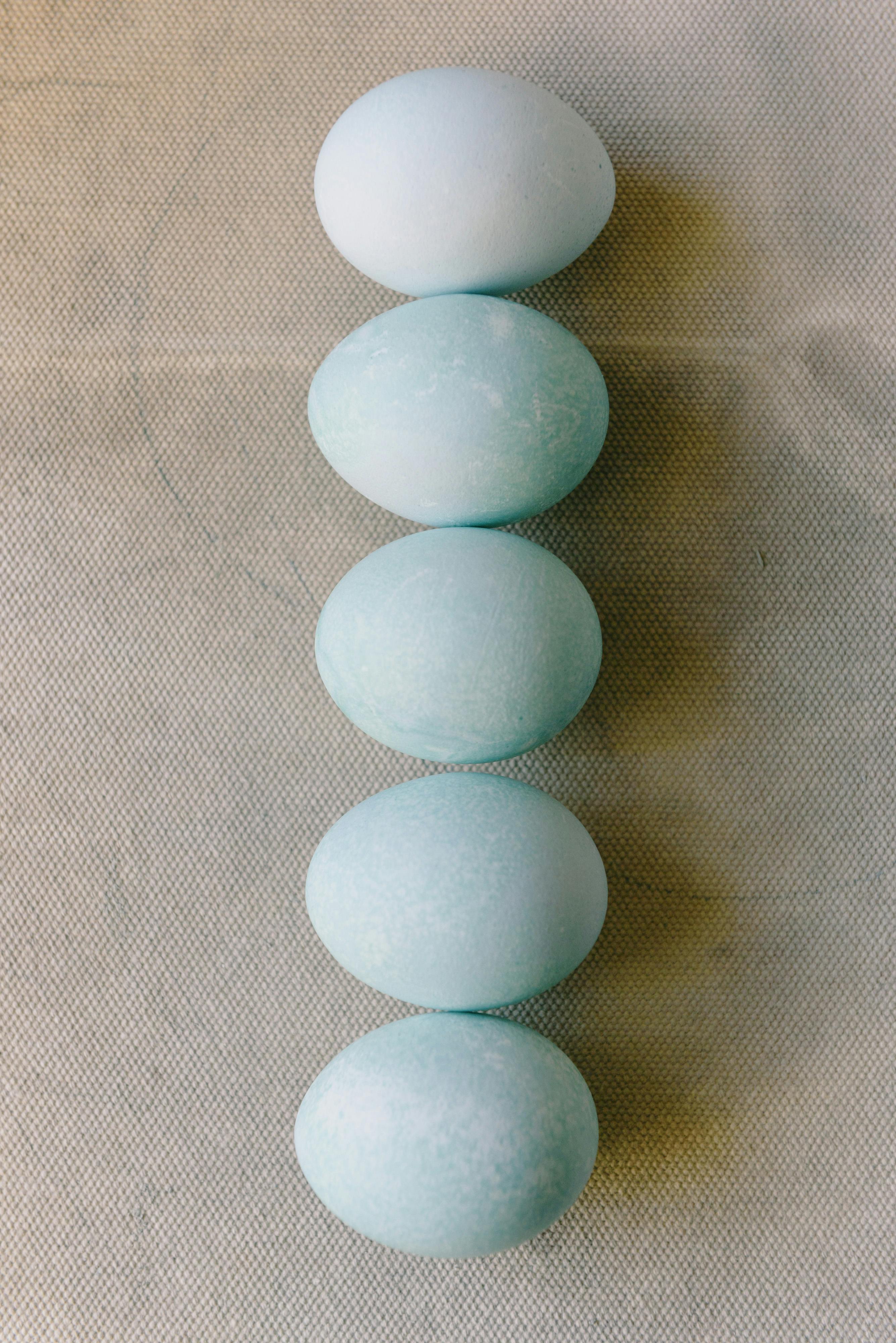 Simple arrangement of blue Easter eggs in a vertical line on a textured surface, perfect for seasonal themes.