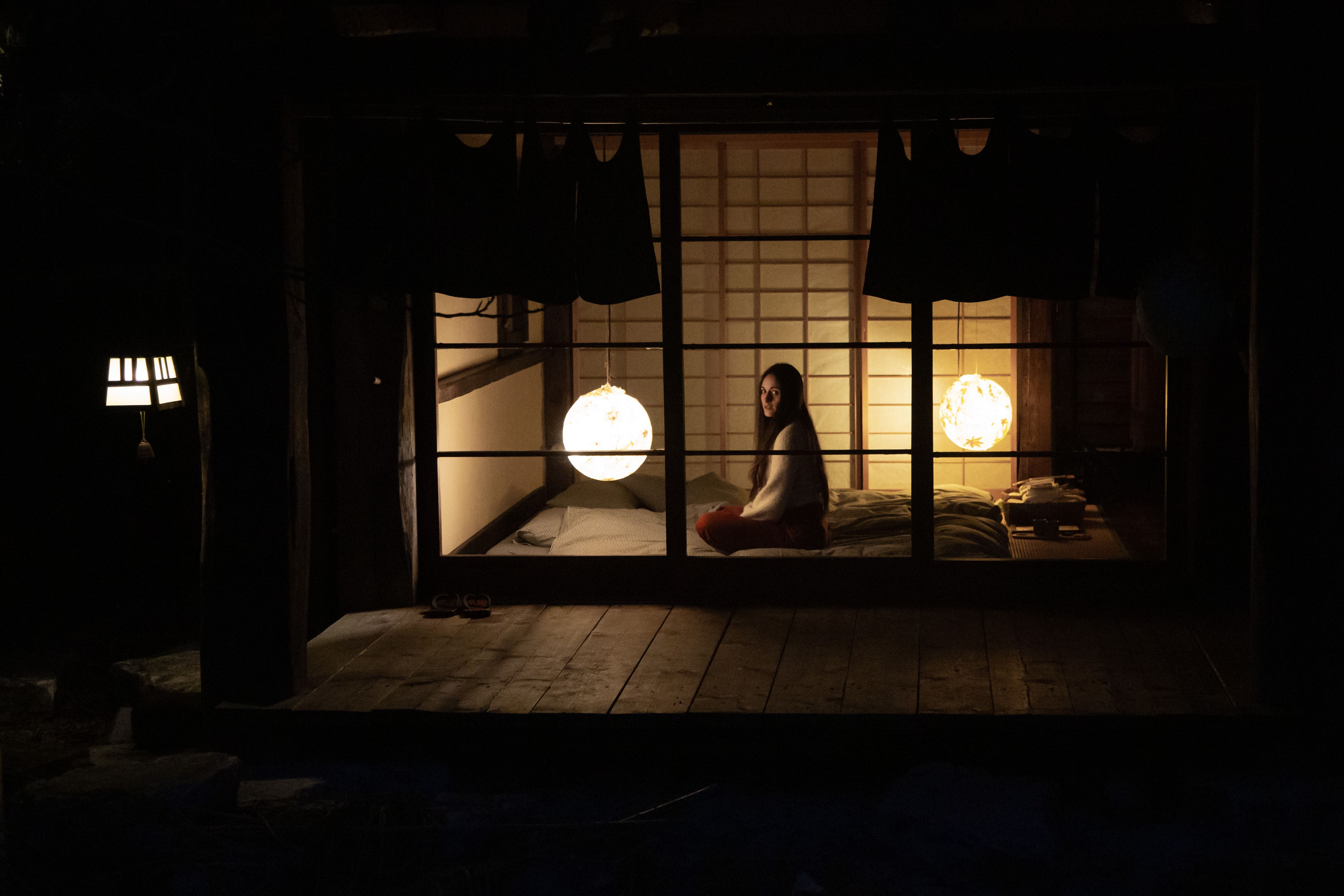 A woman sits peacefully in a softly lit traditional Japanese room, creating a serene and contemplative atmosphere.