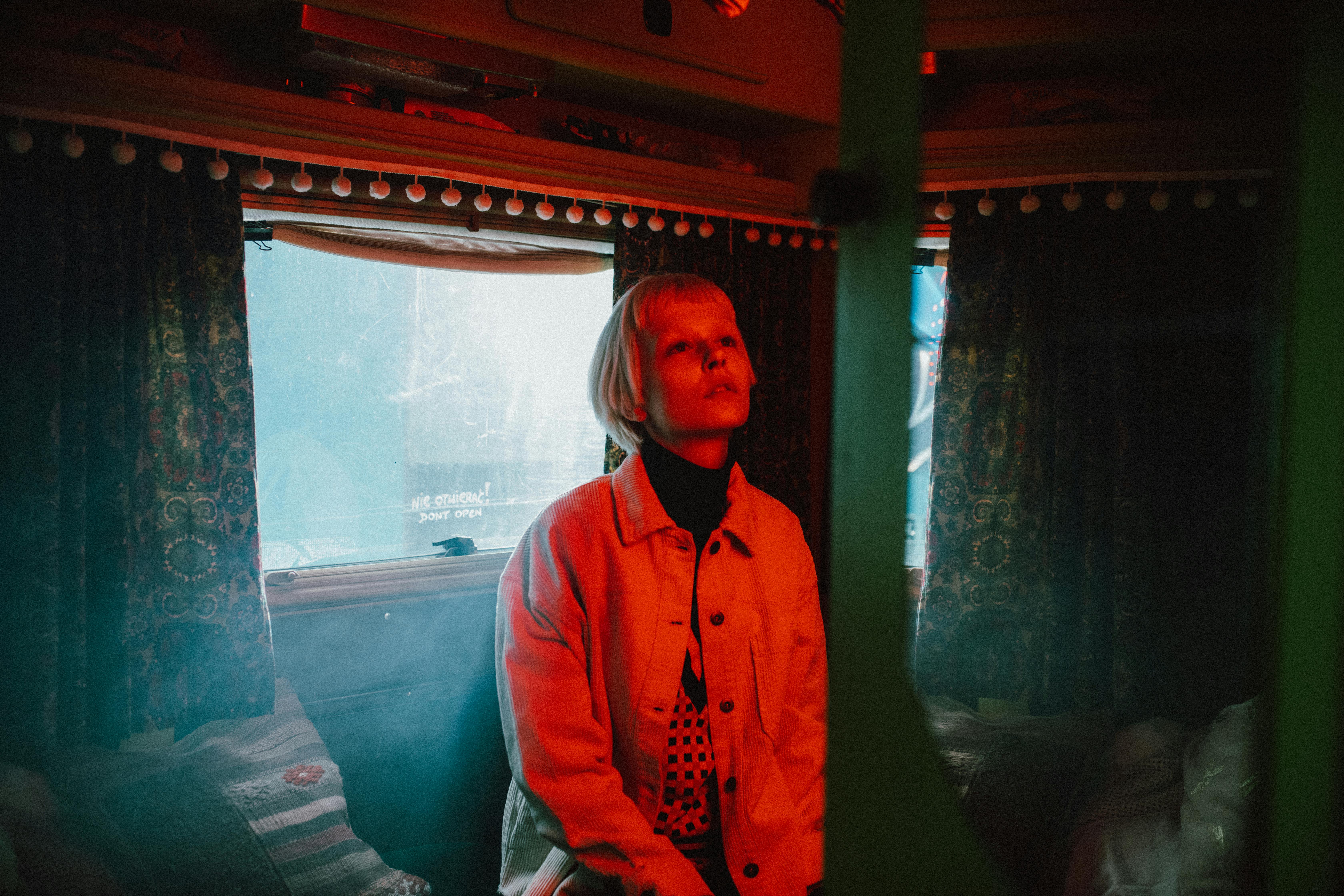 Woman in Blue Jacket Standing Near Glass Window