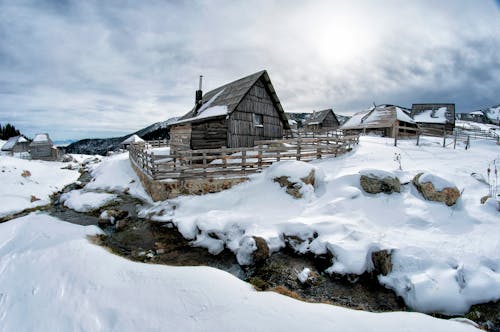 Черный деревянный дом в окружении снега под белыми облаками