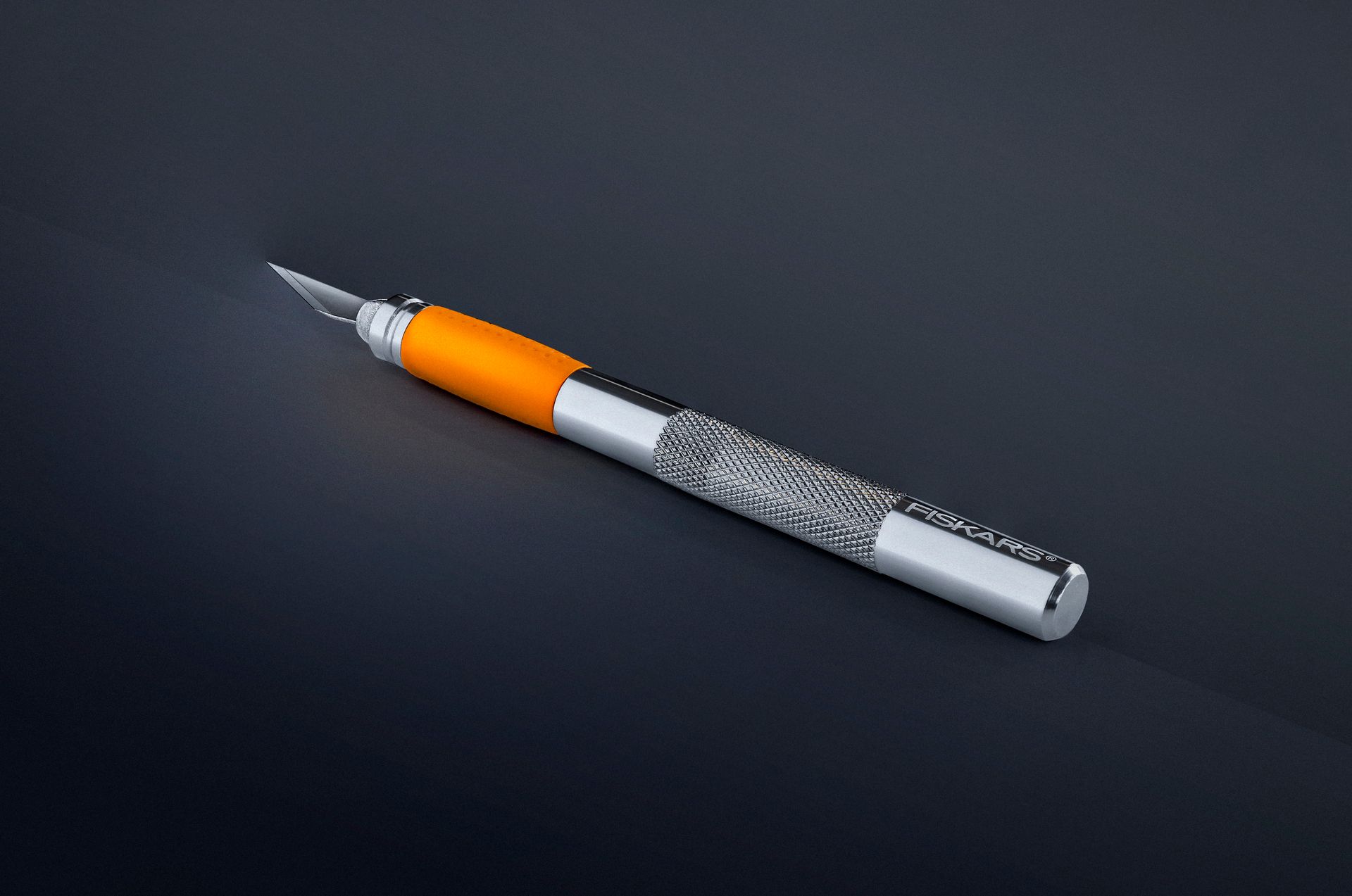 Sharp craft knife with orange and silver handle on a dark studio background.