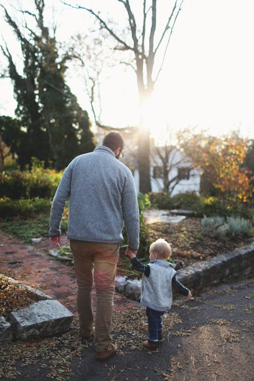 Free Man Holding Hands With Baby While Walking Through Pathway Facing Sunlight Stock Photo