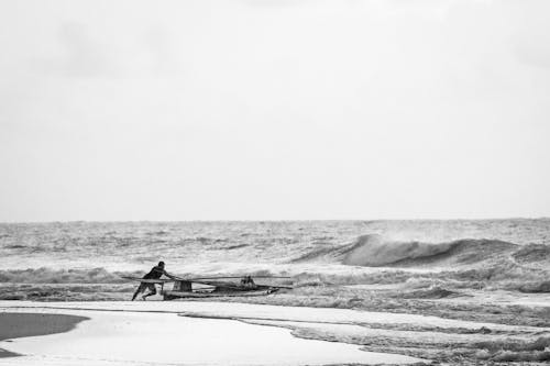 Grayscale Photo of a Man Pushing a Fishing Boat