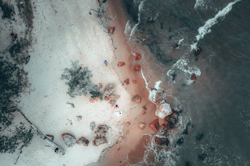 Aerial view of stone boulders scattered on sandy beach washing by foamy ocean