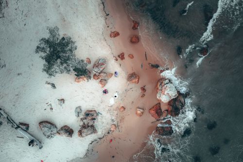 Free Aerial top view of anonymous tourists admiring picturesque wavy ocean rolling on sandy beach and crashing on rocky boulders Stock Photo
