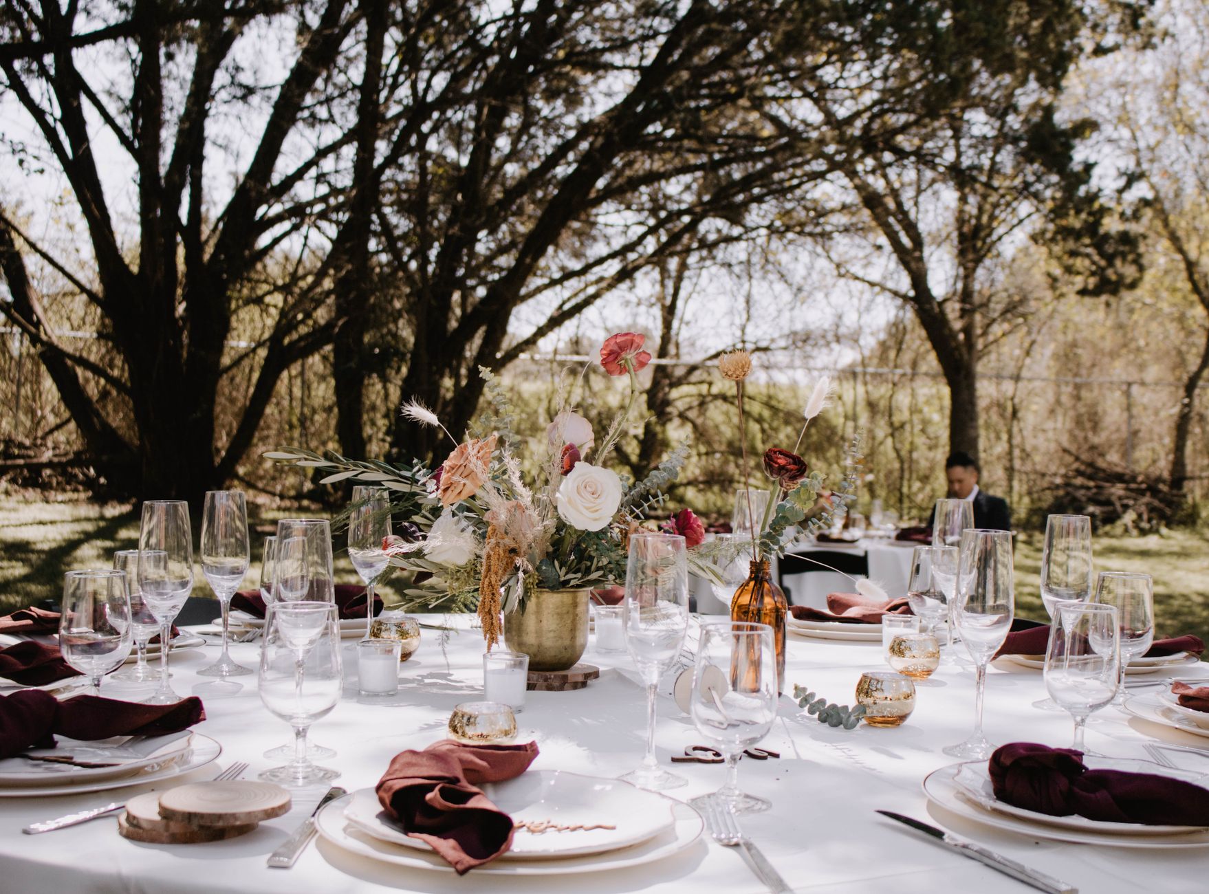 Beautifully decorated outdoor dining table with floral centerpiece, glassware, and tableware for a wedding celebration.