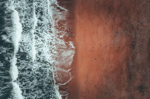 Free Aerial view of anonymous tourists standing on wet sandy seashore near foamy waves during summer holidays Stock Photo