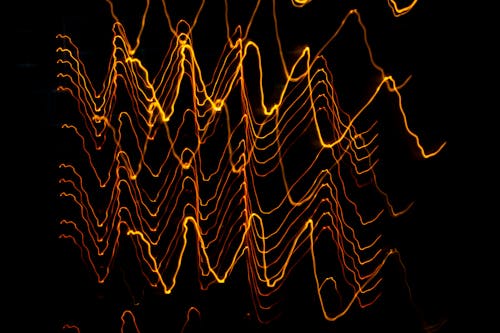 Long exposure of creative modern freezelight light painting with bright wavy lines creating patterns shining on black background in darkness