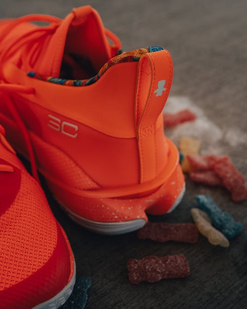 Free Pair of comfy bright orange sneakers placed on dark carpet near scattered marmalade Stock Photo