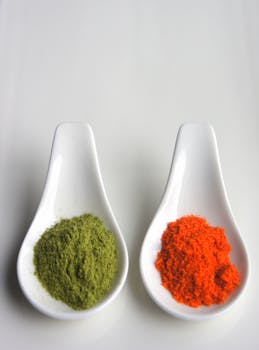 在中性背景上，两个陶瓷勺子盛满了鲜艳的绿色和红色香料粉