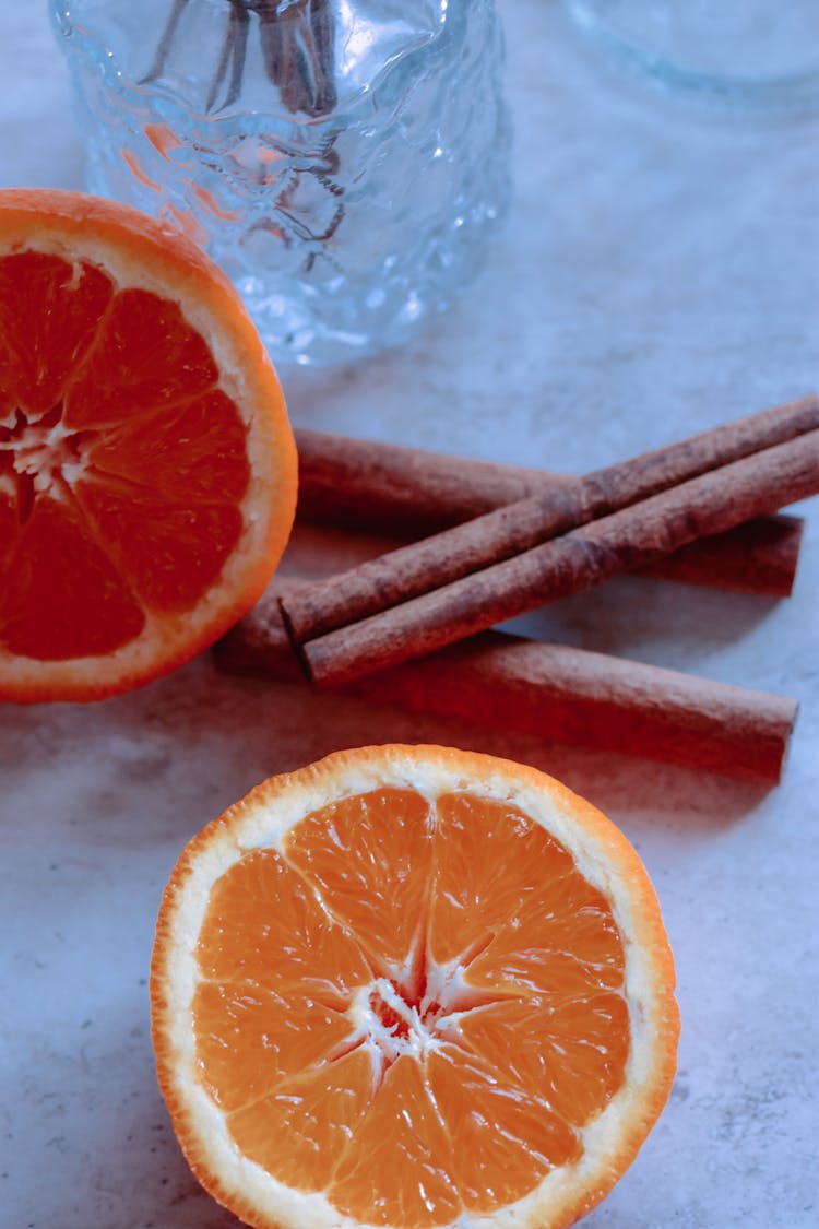 Cut Fresh Orange With Cinnamon Sticks On Table