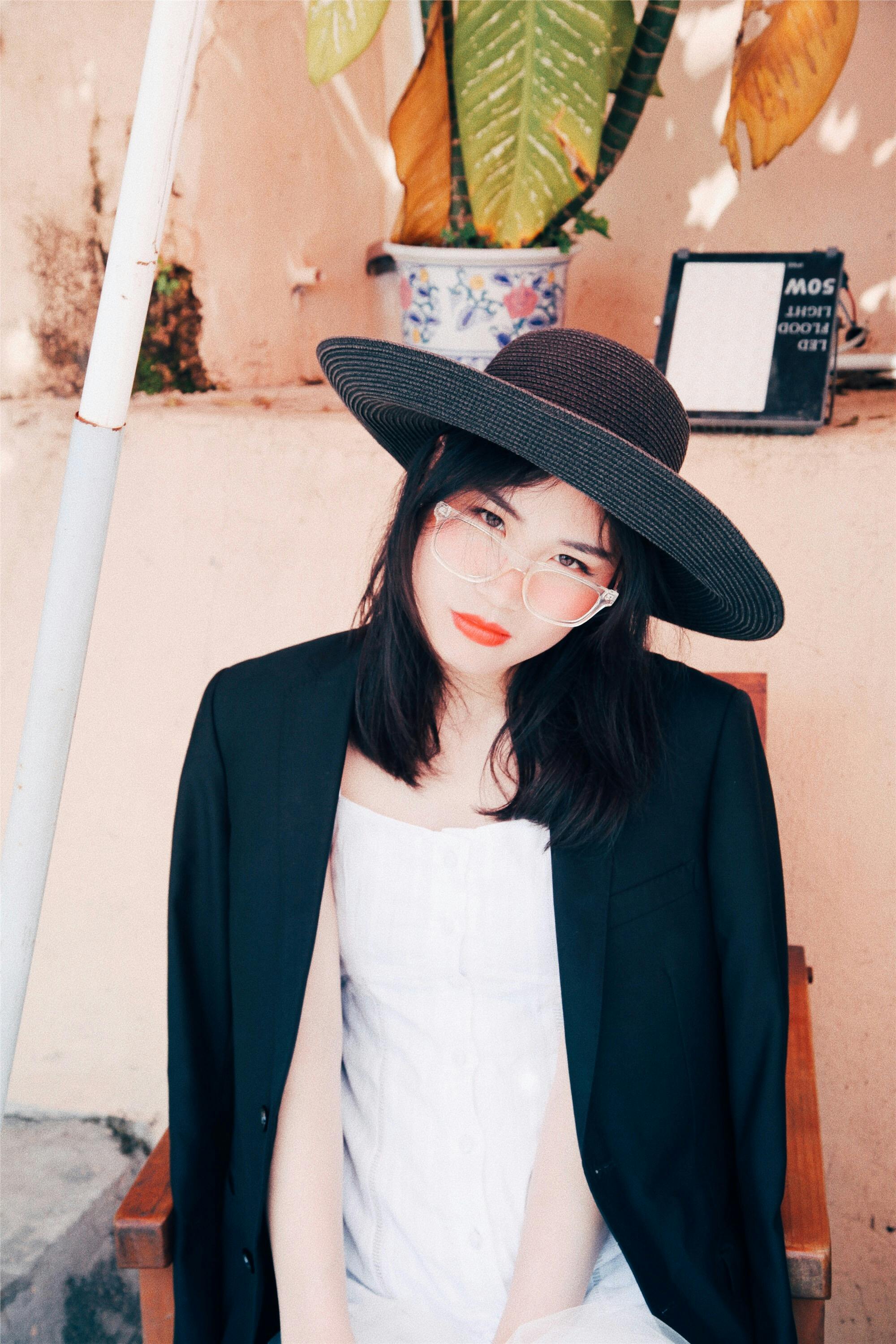 Fashionable woman in black hat and blazer sitting outdoors, showcasing a chic and modern style.