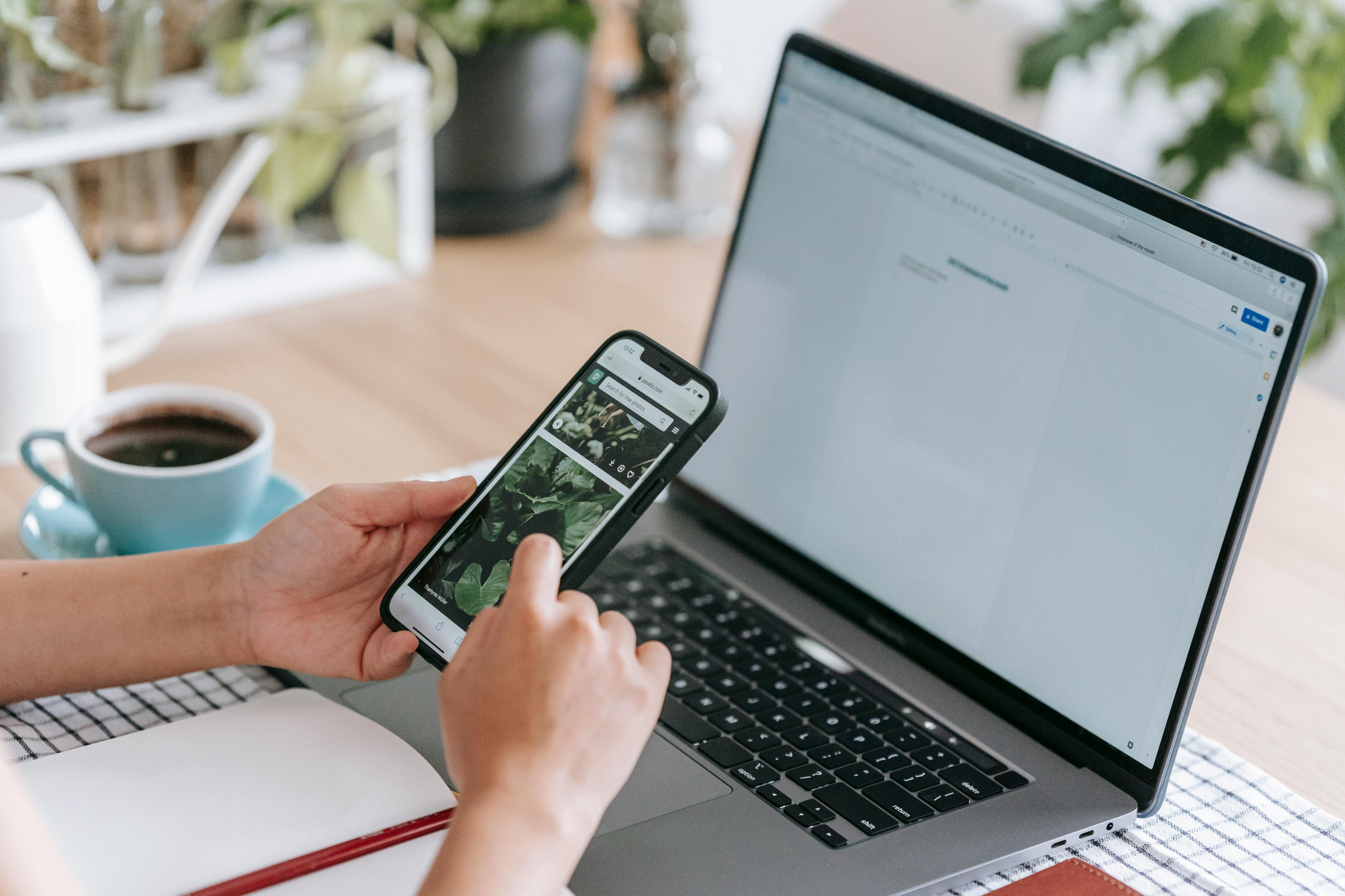 faceless person browsing smartphone near laptop