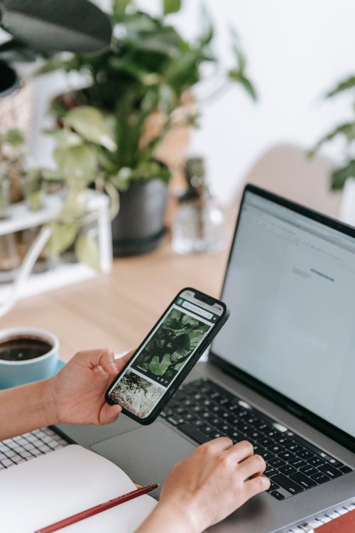 Free Crop unrecognizable person working on netbook and browsing mobile phone while sitting at desk with copybook and cup of coffee in light room Stock Photo