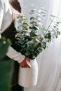 Side view of faceless woman in apron carrying vase with flowering green plant at work in sunlight