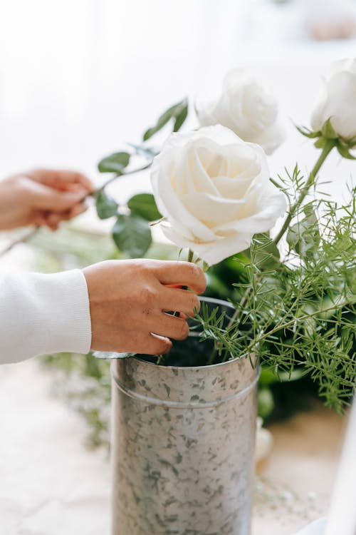 Crop florist making bouquet of blooming roses and plant sprig