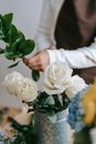 Crop florist making bouquet of blooming roses and Ruscus