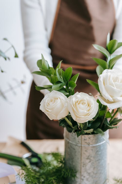 Florist creating bouquet with white roses in iron decorative bucket