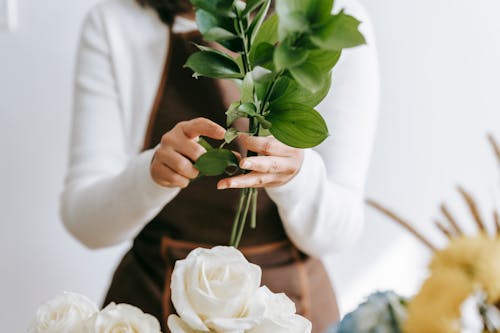 Florist composing bouquet of flowers with green stem and leaves