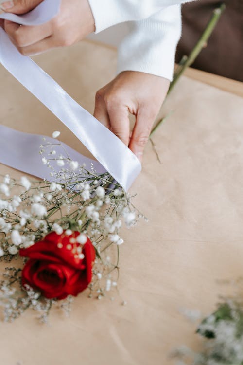 Florist decorating bright red rose with white ribbon · Free Stock Photo