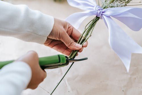 From above of crop anonymous florist cutting green stems of flowers in bouquet against light table