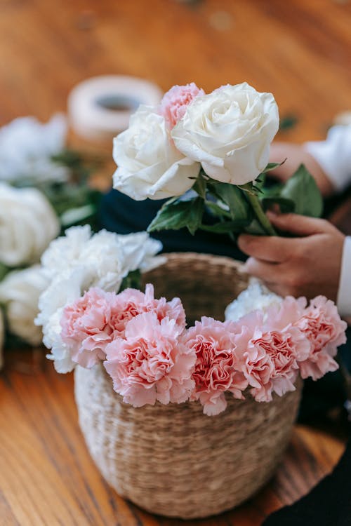 Free From above of crop florist arranging roses and chrysanthemums in wicker basket while making bouquet in light room Stock Photo