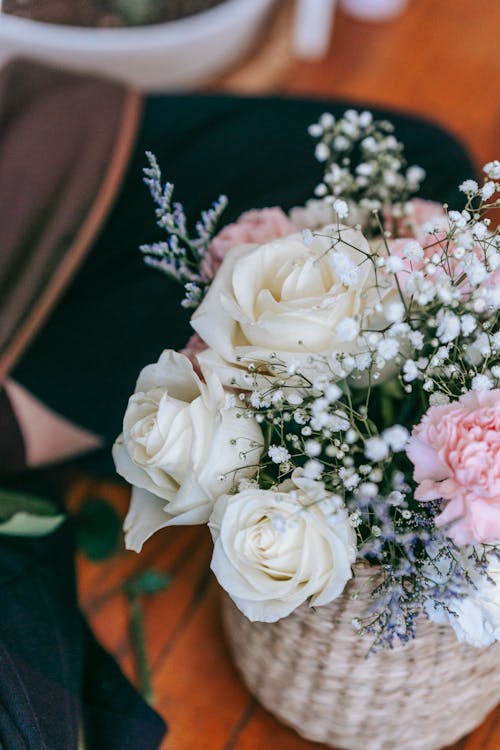 From above of bouquet with aromatic white roses and colorful chrysanthemums placed in wicker basket in daylight