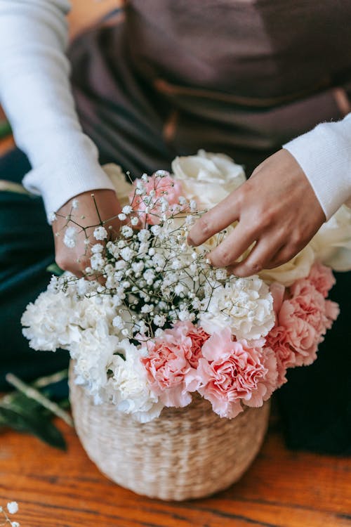 From above of crop anonymous florist arranging bouquet of gypsophila and pink and white roses in wicker basket