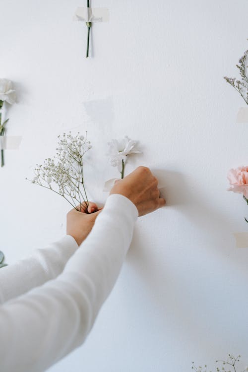Crop decorator gluing flowers to white wall