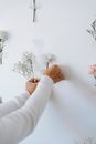 Crop decorator gluing flowers to white wall