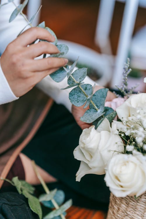 Crop florist inserting flower into bouquet of white roses