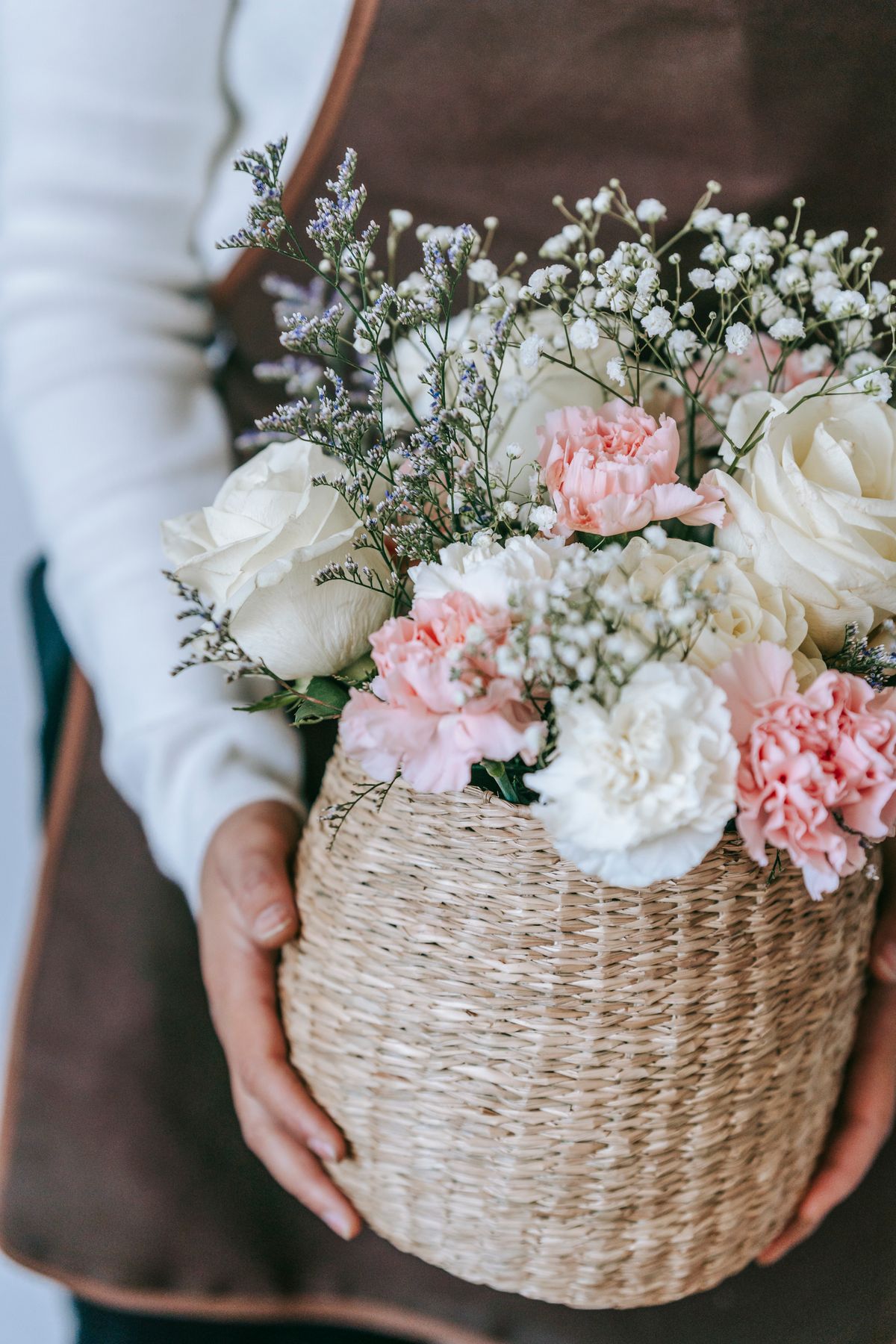 Florist in apron carrying a wicker basket of fresh roses and gypsophila