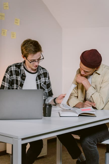Two colleagues brainstorming in a modern office with a laptop and documents.