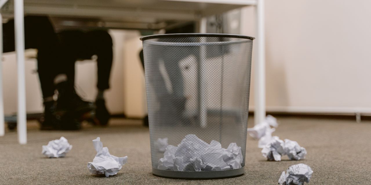 Office floor with a visible trash bin and crumpled papers scattered around, blurring human figures.