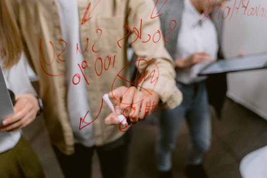 Business team brainstorming with red pen on a glass whiteboard in an office setting.